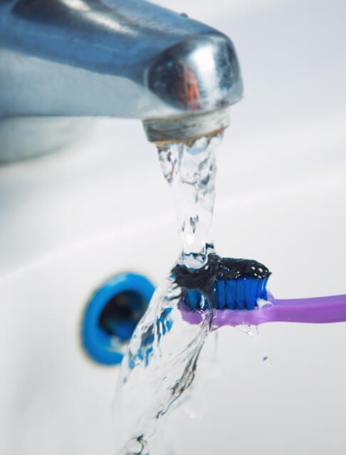 Toothbrush with black toothpaste being rinsed under running water in sink