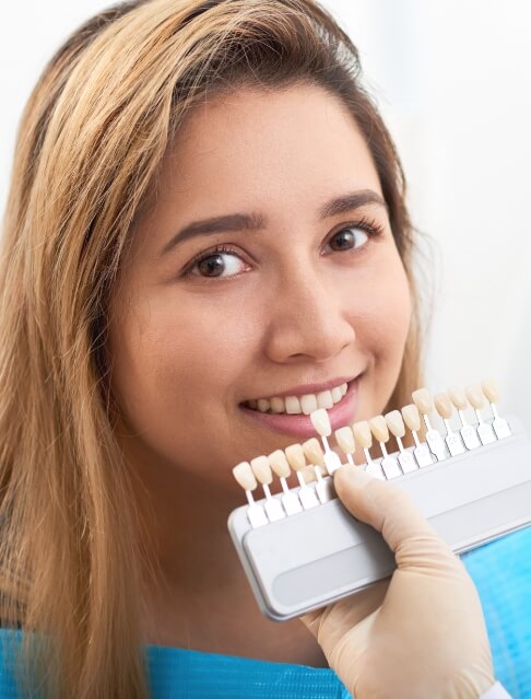 Cosmetic dentist holding shade guide next to a smiling dental patient