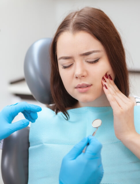 Woman in dental chair holding her cheek in pain