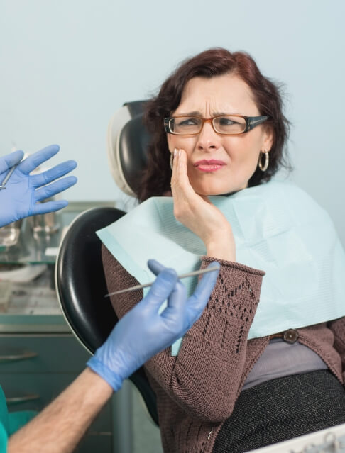 Woman touching her cheek and wincing while talking to dentist