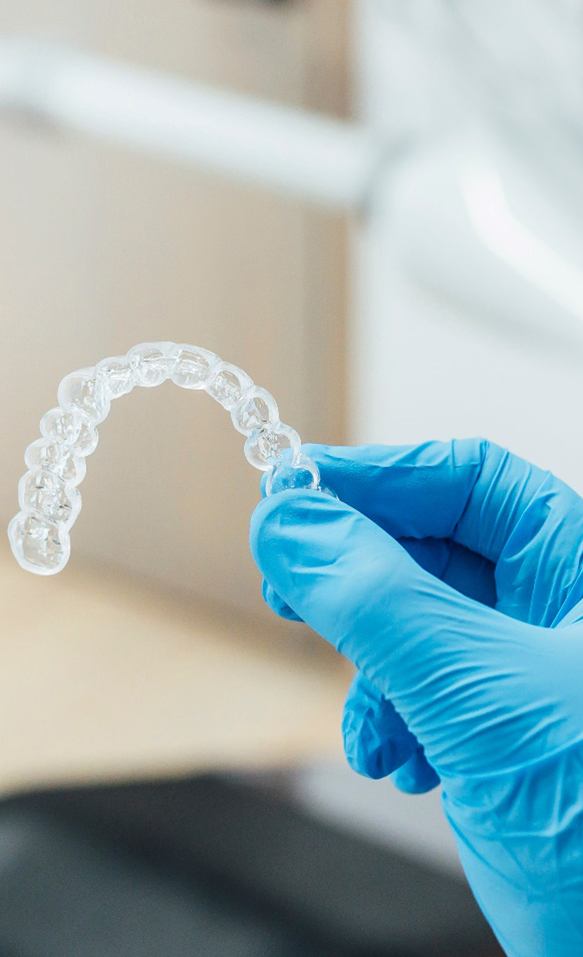 Smiling woman holding Invisalign clear aligner