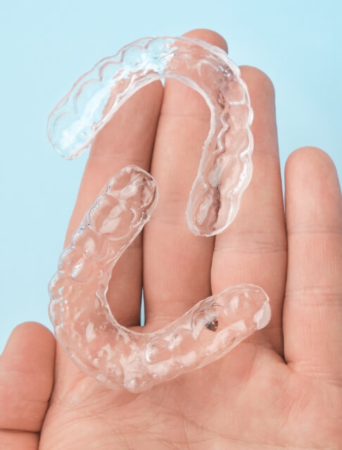 Hand holding two Invisalign clear aligners