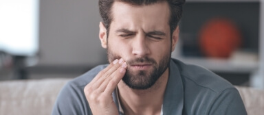 Man in gray polo shirt holding his cheek in pain