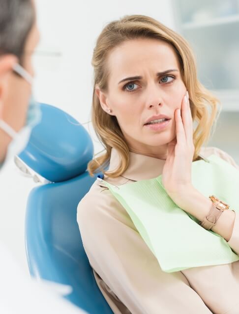 Woman in dental chair touching her cheek in pain